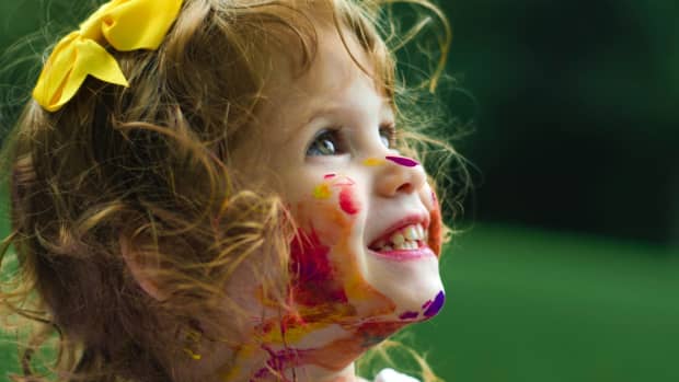 toddler govered in messy red paint, looking very happy about it.