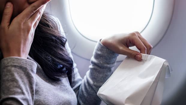 Woman airplane passenger covering mouth with hand and holding full barf bag