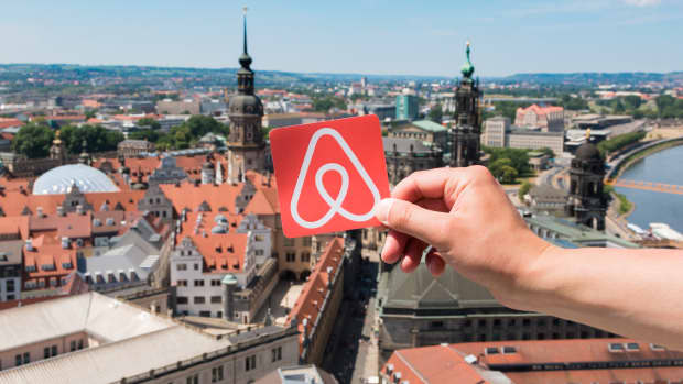 A person holding the Airbnb logo over a high-up view of Dresden, Germany