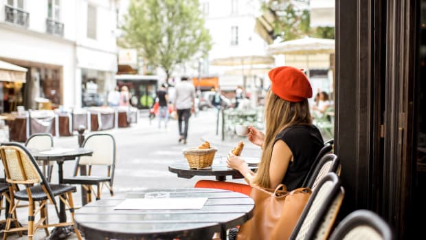 A young woman in a red beret with her back to the camera sits at a Parisian cafe