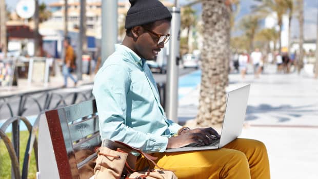 A man works from his laptop while sitting near the beach