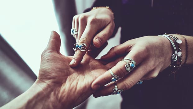 a woman wearing lots of rings on her hands reads someone's palm