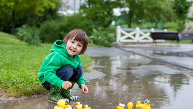 little boy playing in rain with rubber ducks