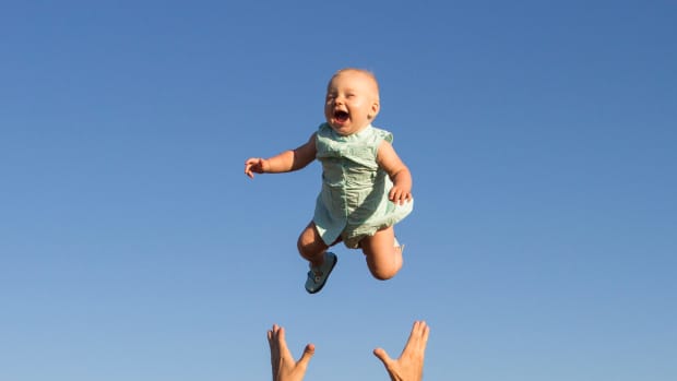 a baby flies in the air with an adults hands reaching up from beneath