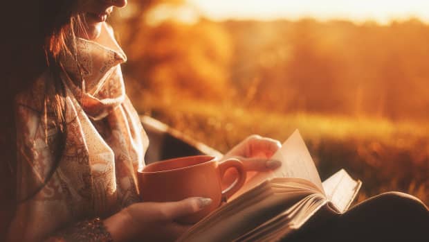 Girl in autumn clothing reading a book at sunset with mug