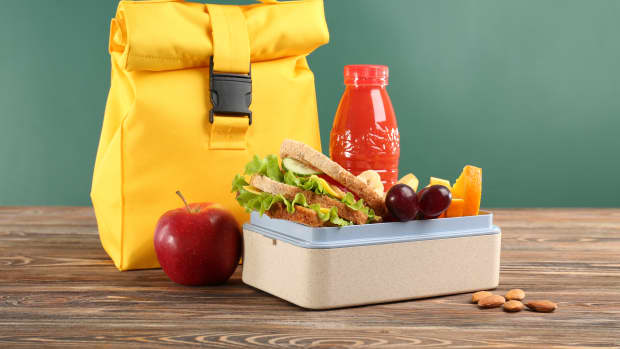 Lunch box with appetizing food and bag on wooden table against chalkboard background