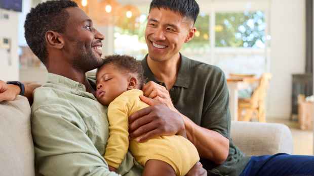 Two men smile while holding a sleeping baby