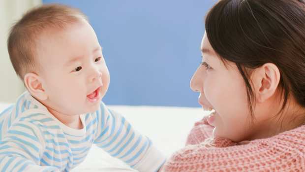 A baby and mom smile at one another while the baby coos