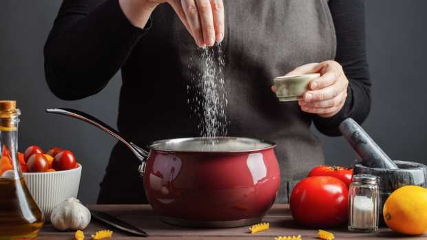 A chef salts a pot of pasta water.