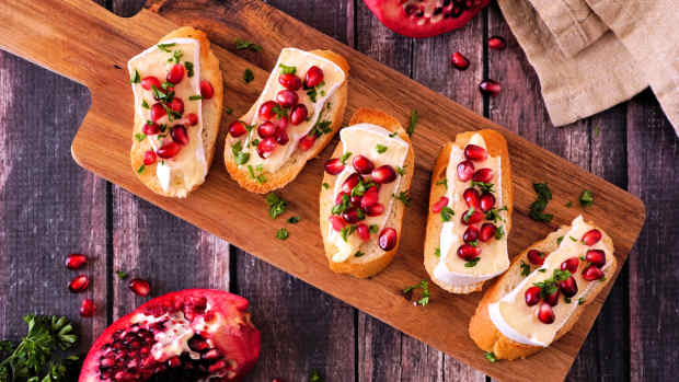 A wooden cutting board with pomegranate and brie crostini.