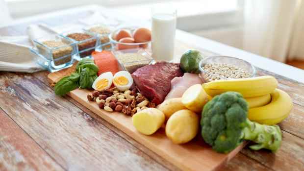 A cutting board with raw meats, nuts, eggs, bananas, potatoes, and vegetables.
