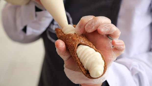 A man is piping cream into a cannoli.