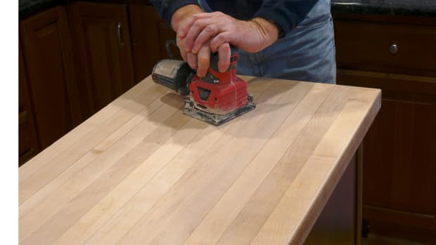 man sanding and refinishing tabletop with hand sander