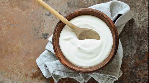 A bowl of homemade sour cream on top of a dish towel, with a wooden spoon inside.