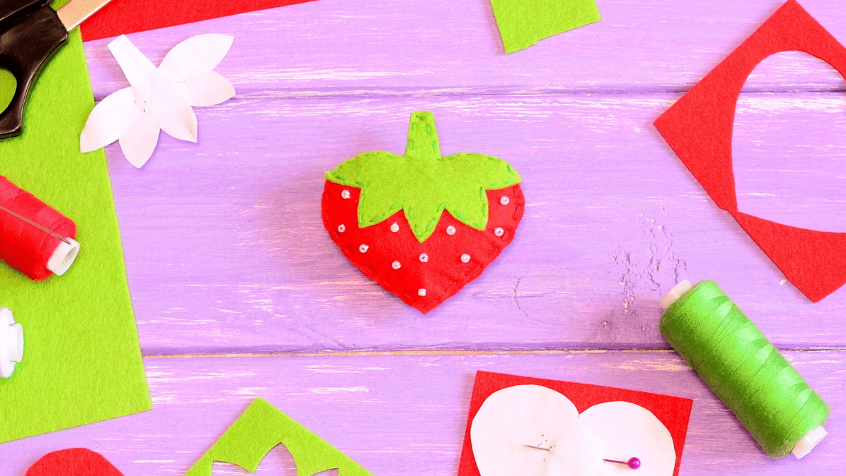 Sewing Handicraft Background. Felt Strawberry Toy, Scissors, Red And Green  Felt Sheets And Scraps, Thread, Needle, Paper Pattern, Beads On Wooden  Background. Cardboard Sheet With Copy Space. Top View Stock Photo, Picture