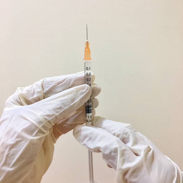 Gloved hand holding needle and syringe.