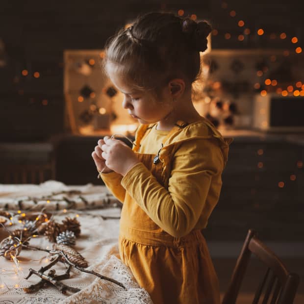 A cute sweet girl makes Christmas decorations from dried oranges, twigs, and cones.