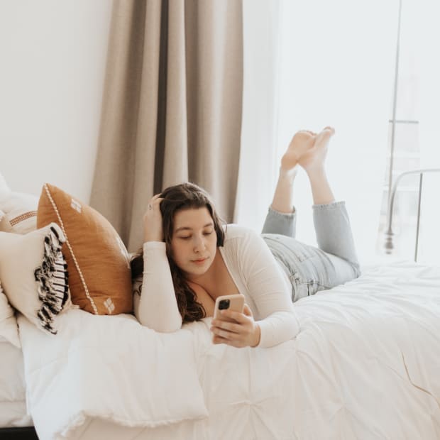 Girl lies on bed with her feet up and looks at her phone.