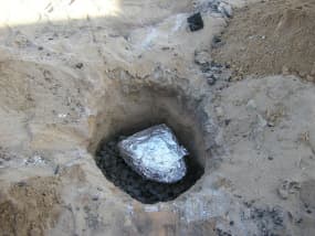 før du senker fuglen i gropen din, må du skyve et lag med varmt trekull på toppen av steinene på bunnen av gropen din. 