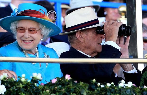 The Queen smiles during a day at the races while the Duke of Edinburgh uses binoculars to watch the field  of horses 