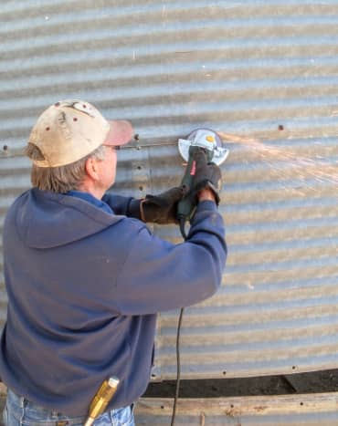 An angle grinder is used to remove stubborn bolt heads on this 1940s era grain bin which is to be moved.