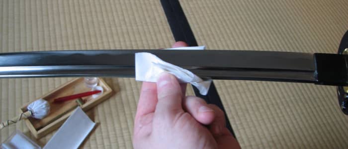 Wiping away the old oil on a katana with a sheet of nuguigami. Sharp edge of the blade facing away, wiping always from hilt to tip.