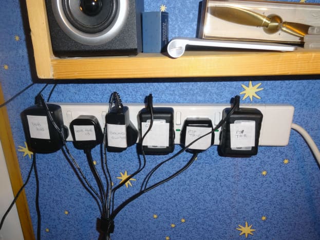 One of the three 6-gang (individually switched) 13Amp wall mounted extension sockets above the desk populated with plugs.