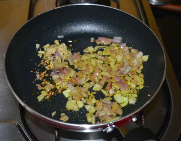 Heat oil in a deep-bottomed pan or wok. Throw in the mustard seeds and let them crackle. Add white lentils and saut&eacute; for 30 seconds. Throw in the grated ginger, chopped onions, and turmeric powder.
