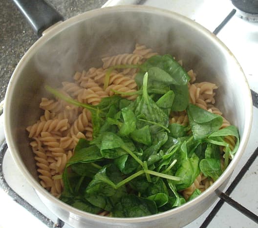 Baby spinach leaves are added to steaming hot pasta