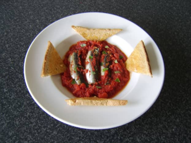 Fresh sardines cooked in homemade tomato sauce are served with hot, buttered toast.