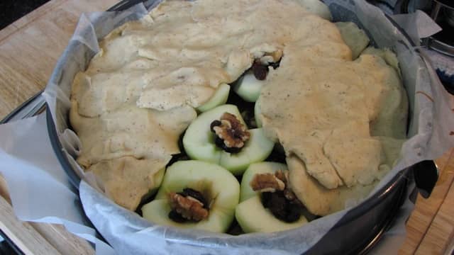 Apples covering toffee, cut sides up, filled with sultanas and walnuts. Flattened pieces of dough covering apples.