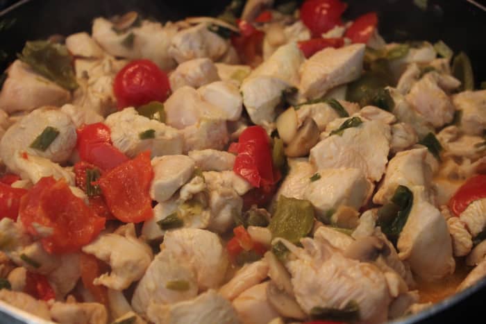 Chicken cooking with cherry peppers, garlic, scallions and mushrooms.