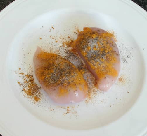 Turmeric and black pepper are scattered over chicken breasts