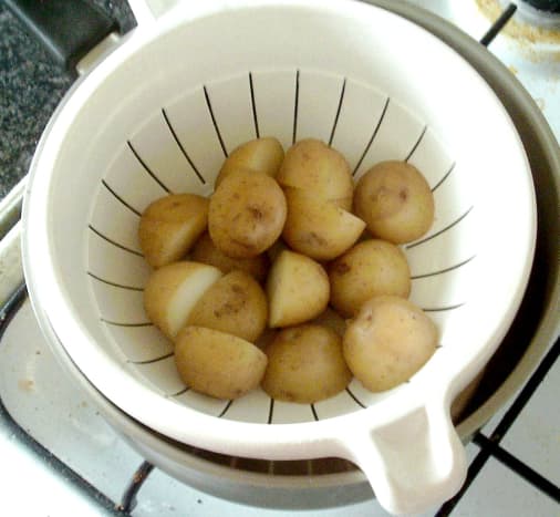 Halved potatoes are cooked by boiling then drained and allowed to steam off and cool