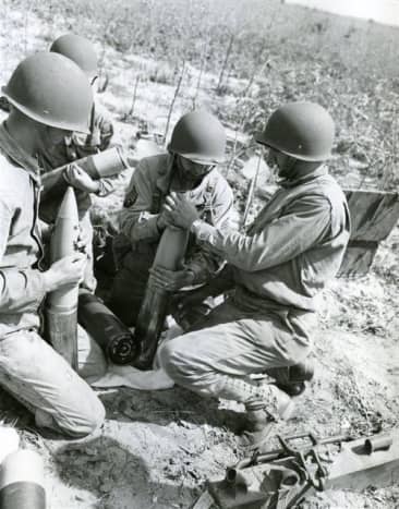 105mm crew preparing the shells during training exercise. Ft. Jackson, 1943. The sergeant in the middle is instructing the soldier on attaching the shell (top part) to the casing below after it has been packed with ammo bags.