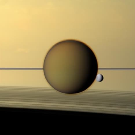 Saturn's moon Titan, 3200 miles across, and Dione, 698 miles across, float against the backdrop of Saturn's cloud tops and rings. Look closely; you can see Titan's fuzzy atmosphere in front of Dione.