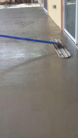 As the concrete was poured into each section of the patio, a worker with a very long pole smoothed the surface. 