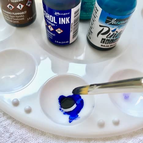 Mixing ink colors on a small plastic paint palette with a paint brush.
