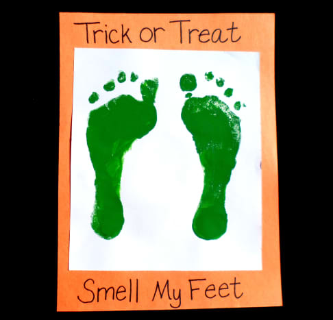 Add green footprints to a white sheet of paper with the title &quot;Trick or Treat, Smell My Feet&quot;.