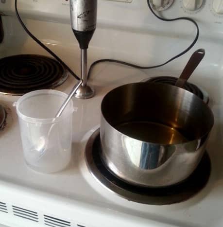 The lye and water mixture in the small plastic container sits next to the pan of melted coconut oil. Now all you have to do is add the lye-water to the oil.