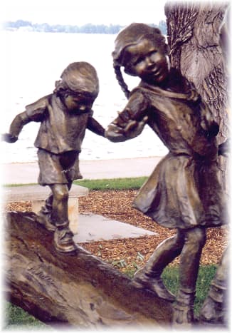Partial view of a sculpture where 5 children are balancing themselves as they make their way across a log.