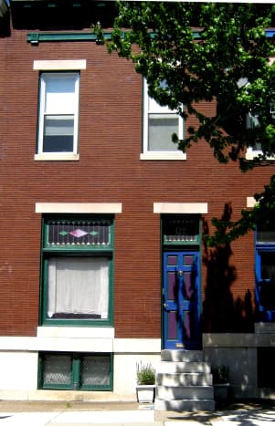 This 2 bay, 2 story rowhouse still has its stained glass above the window and front door.