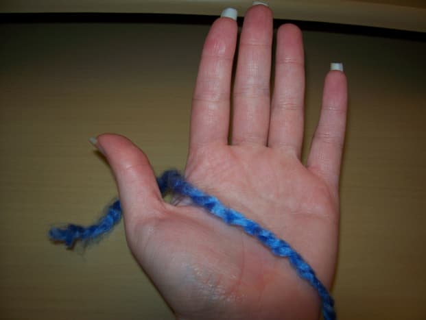 Palm facing you, yarn between thumb and pointer finger, tail behind hand.