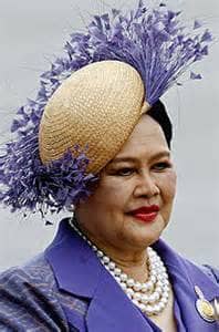 Queen SiriKit (Queen of Thailand) wearing a multi-strand pearl necklace with a white hat and purple plumes and a purple suit