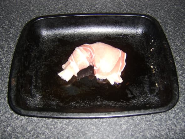Chicken is wrapped in bacon and placed on an oiled baking tray
