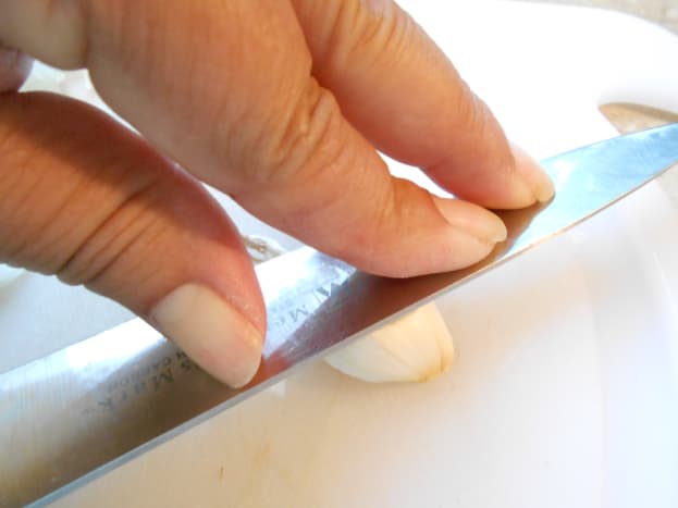 Place garlic clove in skin onto cutting board.  With your fingers, press down firmly on the flat side of your knife two or three times.  You will hear the skin of the garlic crack.