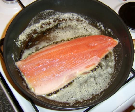 The trout fillet is laid in a hot pan with the skin side down.