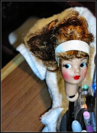 Next, I began to work on the head.  Tammy received a rubber band hair band to set her bangs in place.  The head was propped up with an eraser pen to check out the damage and make sure the head was in a good position to be completely dry.  Glue adhere