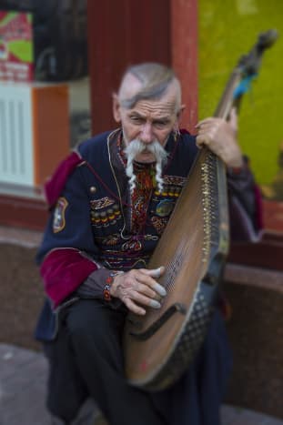 A Ukrainian wearing traditional garb, playing the bandura (a Ukrainian, plucked string, folk instrument)