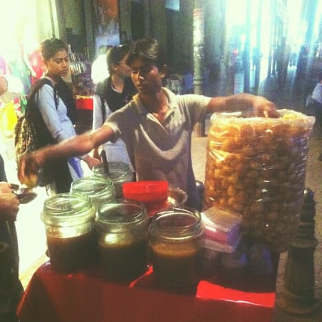 A vendor with the round puris and the different flavored water in different containers in front of him